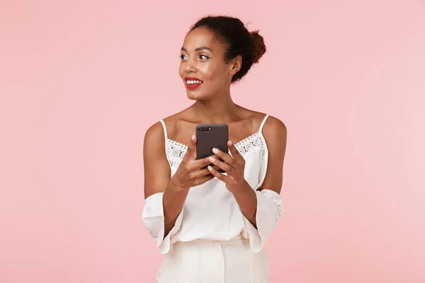携帯電話を用いたピンク背景の壁に分離された美しい若いアフリカ女性のイメージ — ストック写真