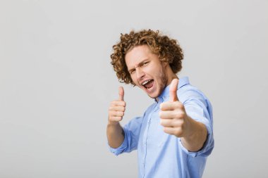 Yaşasın vererek gri arka plan üzerinde izole ayakta gömlek giymiş mutlu bir genç adam portresi