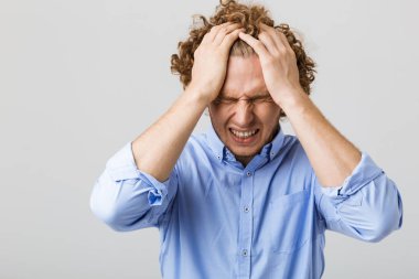 Bir baş ağrısı acı gri arka plan üzerinde izole gömlek ayakta giyen umutsuz genç bir adam portresi