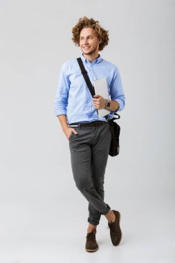 Taşıma çantası ve laptop beyaz arka plan üzerinde izole ayakta gülümseyen genç işadamı tam uzunlukta