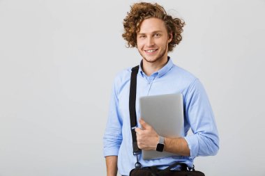 Genç işadamı beyaz arka plan üzerinde izole ayakta taşıma çantası ve dizüstü gülümseyen