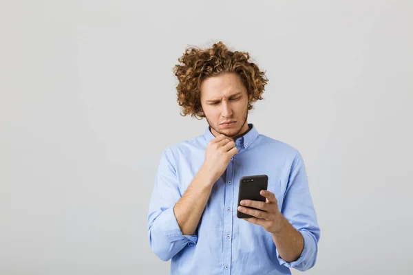 一个沉思的年轻人的肖像与卷发查出在白色背景 拿着手机 — 图库照片