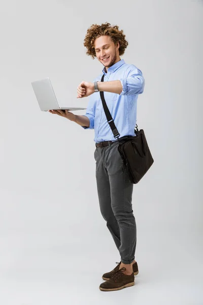 笑顔若いビジネスマンの分離に立って白い背景に キャリング バック ノート パソコン 腕時計を見て完全な長さ — ストック写真