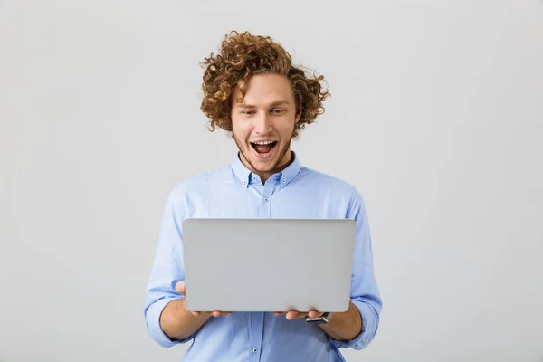 陽気な若い男が分離灰色の背景の上に立っているシャツを着て見てラップトップ コンピューターの肖像画 — ストック写真