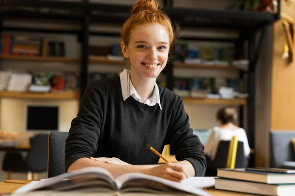 Sorrindo Menina Adolescente Cabelos Vermelhos Estudando Mesa Biblioteca — Fotografia de Stock