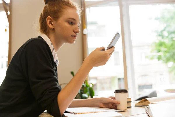 Adolescente Pelirroja Concentrada Estudiando Mesa Biblioteca Tomando Café Usando Teléfono —  Fotos de Stock