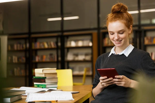 Sorrindo Menina Adolescente Cabelos Vermelhos Estudando Mesa Biblioteca Usando Telefone — Fotografia de Stock