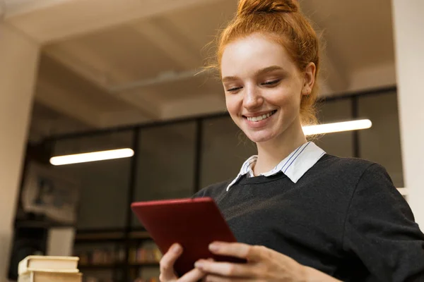 Cep Telefonu Kullaranarak Kütüphanede Okuyan Kırmızı Saçlı Genç Kız Gülümseyerek — Stok fotoğraf