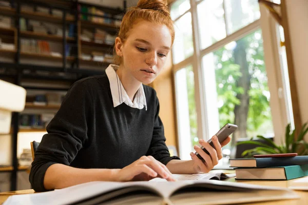 Adolescente Pelirroja Concentrada Que Estudia Mesa Biblioteca Con Teléfono Móvil —  Fotos de Stock