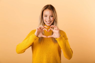 Çok güzel bir genç kadının portresi sevgi jest gösterilen sarı arka plan üzerinde izole ayakta kazak giymiş