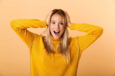 Sürpriz bir genç kadının portresi çığlık, sarı arka plan üzerinde izole ayakta kazak giymiş