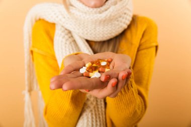 Bir kadının hap izole sarı duvar arka plan üzerinde tutan eşarp resim kırpılmış.