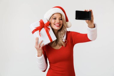 Mutlu sarışın bir kadın portresi hediye kutusu, bir selfie alarak holding beyaz arka plan üzerinde izole duran kırmızı yılbaşı kostüm giymiş