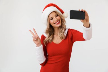 Çok mutlu sarışın bir kadın portresi bir selfie alarak, beyaz arka plan üzerinde izole duran kırmızı yılbaşı kostüm giymiş