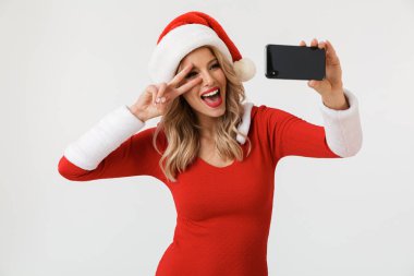 Pozitif sarışın bir kadın portresi bir selfie alarak, beyaz arka plan üzerinde izole duran kırmızı yılbaşı kostüm giymiş