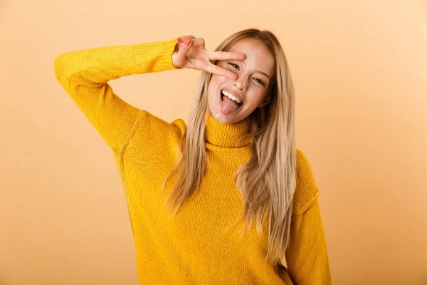 平和のジェスチャーを示す黄色の背景に分離立ってセーターに身を包んだ面白い若い女性の肖像画 — ストック写真