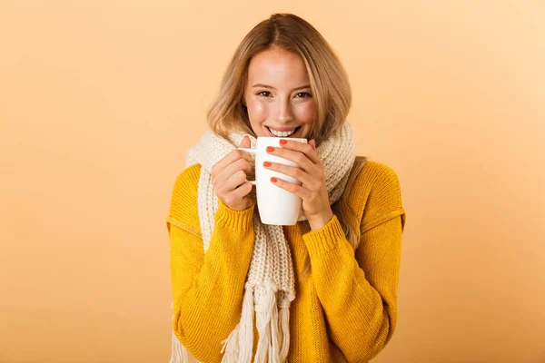 スカーフは 黄色の壁の背景に分離されたポーズを着てお茶のカップを保持している かわいいきれいな女性の写真 — ストック写真