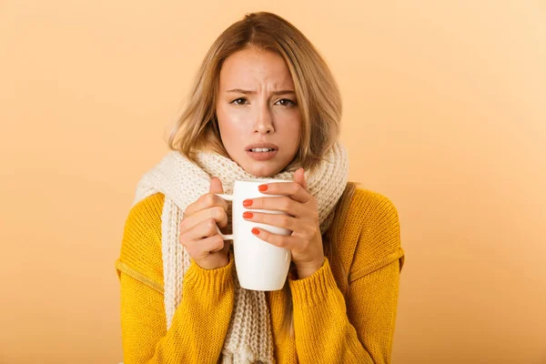 スカーフ ポーズ病気黄色の壁の背景に分離された身に着けているお茶のカップを保持している不機嫌な女性の写真 — ストック写真