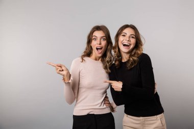 Görüntü gülümseyen ve gri arka plan üzerinde bir kenara birlikte izole parmakları işaret iki sevimli kız