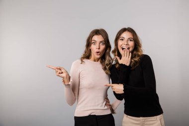 Görüntü gülümseyen ve gri arka plan üzerinde bir kenara birlikte izole parmakları işaret iki pozitif kız