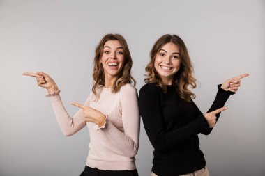 Görüntü gülümseyen ve gri arka plan üzerinde bir kenara birlikte izole parmakları işaret iki güzel kadın