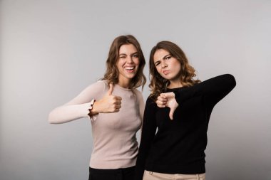 Gri arka plan üzerinde iki neşeli kız başparmak yukarı ve aşağı gösterilen görüntü izole