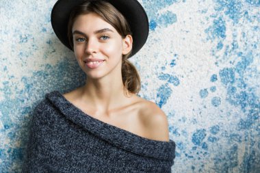 Mavi duvar arka plan üzerinde kazak ve şapka giymiş genç gülümseyen bir kadın portresi yakın poz