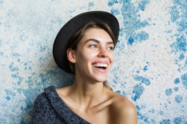 Mavi duvar arka plan üzerinde kazak ve şapka giymiş genç gülümseyen bir kadın portresi yakın poz