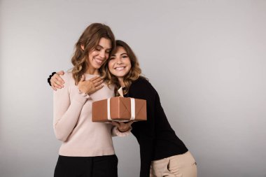 Görüntü gülümseyen ve mevcut kutusu gri arka plan üzerinde izole poz iki neşeli kız