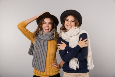 Şapka ve gri arka plan üzerinde izole kamera gülümseyen tulum giyen iki güzel kadın görüntüsünü