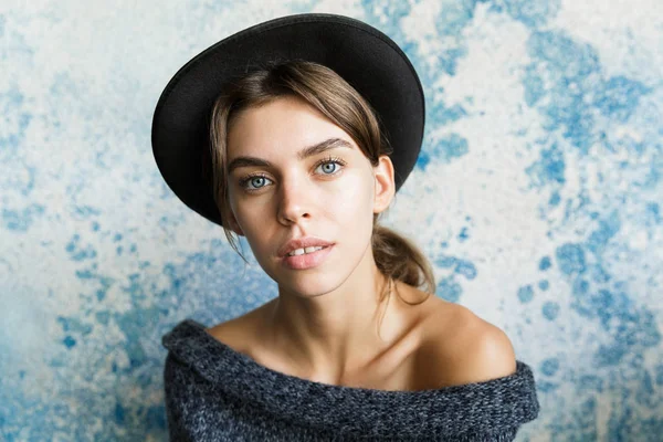 一个年轻女子穿着毛衣 帽子在蓝色墙壁背景下 看着相机的特写镜头 — 图库照片