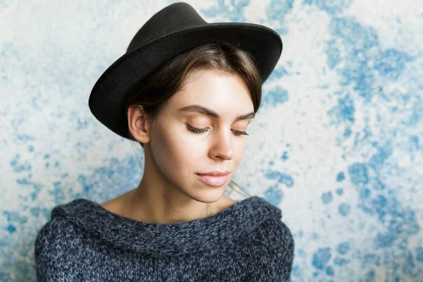 Close up portrait of a beautiful young woman dressed in sweater and hat over blue wall background, eyes closed