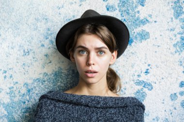 Kameraya bakarak mavi duvar arka plan üzerinde kazak ve şapka giymiş karışık genç bir kadın portresi kapatın