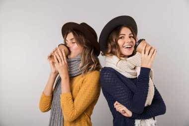 Şapka ve paket servisi olan restoran kahve gri arka plan üzerinde izole kağıt bardak tutan tulum giyen iki pozitif kadın görüntüsünü