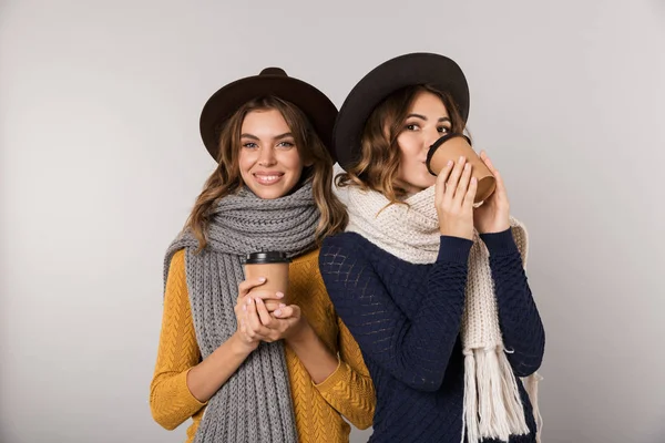 Şapka ve paket servisi olan restoran kahve gri arka plan üzerinde izole kağıt bardak tutan tulum giyen iki Avrupa kadın görüntüsünü