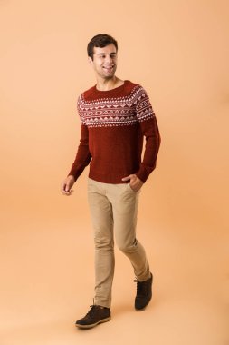 Beyaz adamla 20s tam boy görüntü gülümseyen izole bej renkli arka plan üzerinde yürürken giyen örme kazak kıl