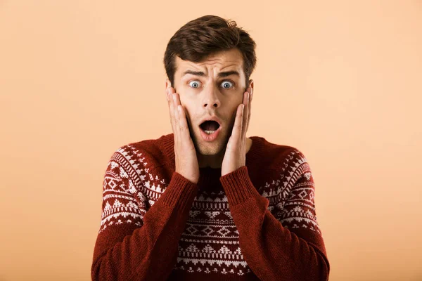 Image of intimidated man 20s with stubble wearing knitted sweater screaming and touching face isolated over beige background