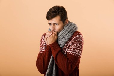 Portre genç bir adam kazak ve bej renkli arka plan üzerinde izole eşarp silah kadar ısınma giyinmiş