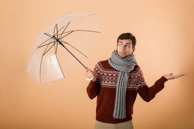 Kazak ve şemsiyesi altında duran bej renkli arka plan üzerinde izole eşarp portre karışık bir genç adam giymiş