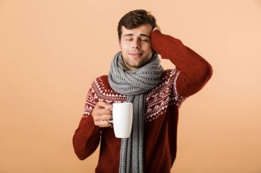 Kazak ve bej renkli arka plan üzerinde izole bir fincan çay içme eşarp giymiş yakışıklı genç