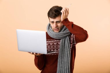 Kazak ve dizüstü bilgisayar tutan tarama, bej renkli arka plan üzerinde izole eşarp portre umutsuz hasta bir adam giymiş