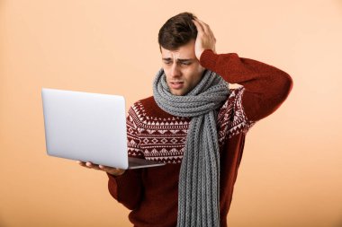 Kazak ve dizüstü bilgisayar tutan tarama, bej renkli arka plan üzerinde izole eşarp portre hasta bir adam giymiş