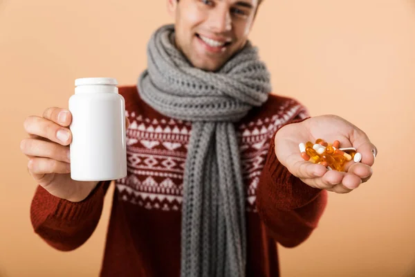 特写肖像一个满意的人穿着毛衣和围巾隔离在米色的背景 显示瓶子和药丸 — 图库照片