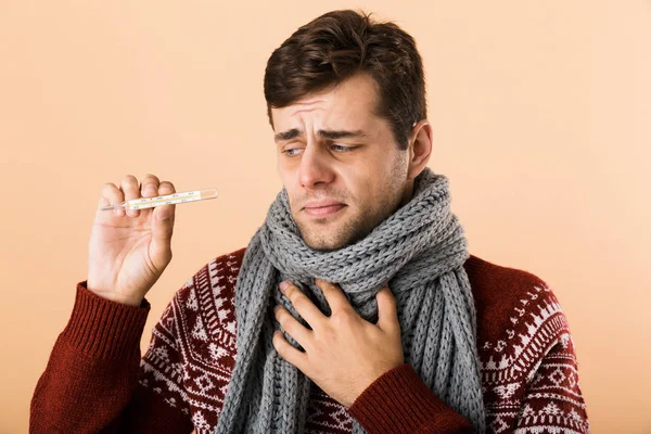 一个悲伤的病人穿着毛衣和围巾的特写镜头 在米色的背景下 显示温度计 — 图库照片
