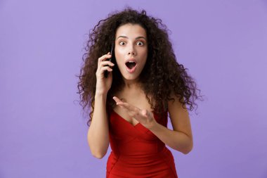 Görüntü izole mor arka plan üzerinde duran siyah cep telefonuyla konuşurken çok mutlu kadın 20'li yaşlarda giyen kırmızı elbise