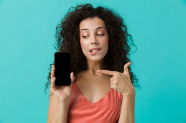 Cep telefonu üzerinde mavi arka plan izole, kıvırcık saçlı işaret parmağı güzel kadın 20'li yaşlarda fotoğrafı