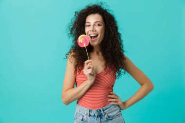 Muhteşem bir kadın 20'li yaşlarda giyiyor rahat giyim üzerinde mavi arka plan izole lolipop tutan portresi