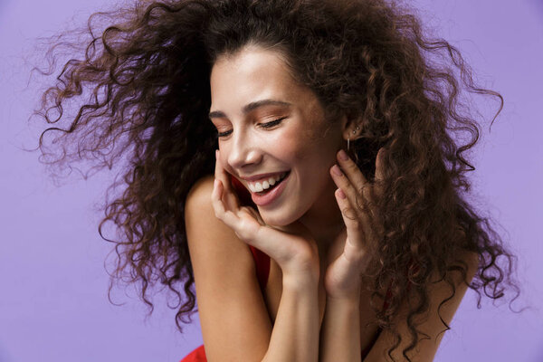 Изображение великолепной женщины 20 лет в красном платье смеется стоя изолированно на фиолетовом фоне
