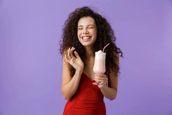 一个满意的女人的肖像与深色卷发穿着红色礼服隔离在紫罗兰色背景 喝奶昔从玻璃 — 图库照片