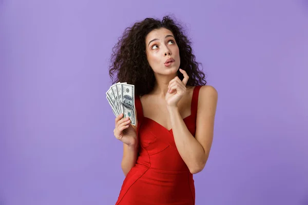 一个沉思的女人的肖像与深色卷发穿着红色礼服隔离在紫罗兰色背景 显示金钱钞票 — 图库照片